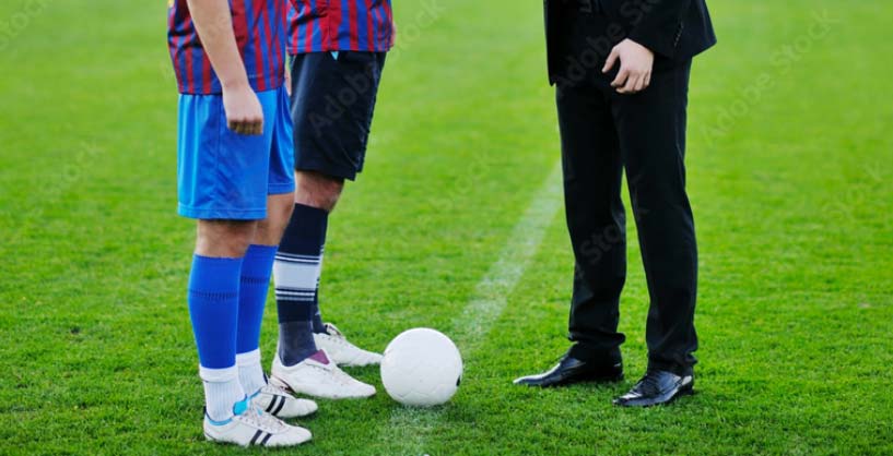 2 football players and a suited man on a football field.