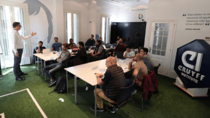 Johan Cruyff Institute classroom with students and a teacher. Johan Cruyff's silhouette can be seen on a wall.